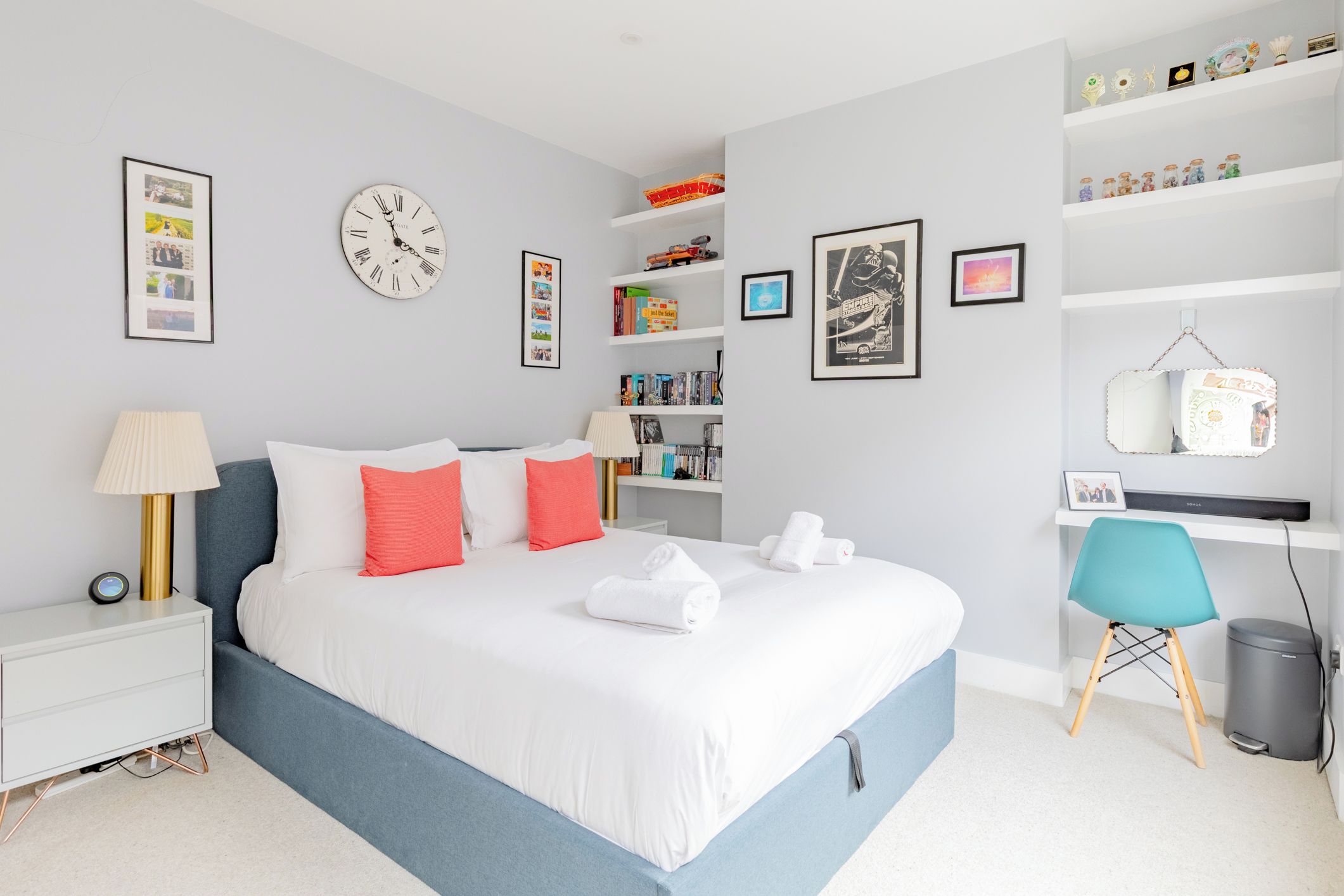 Une chambre à coucher moderne, avec un lit, des tables de chevet, un bureau et des étagères remplies de livres et d’objets décoratifs.