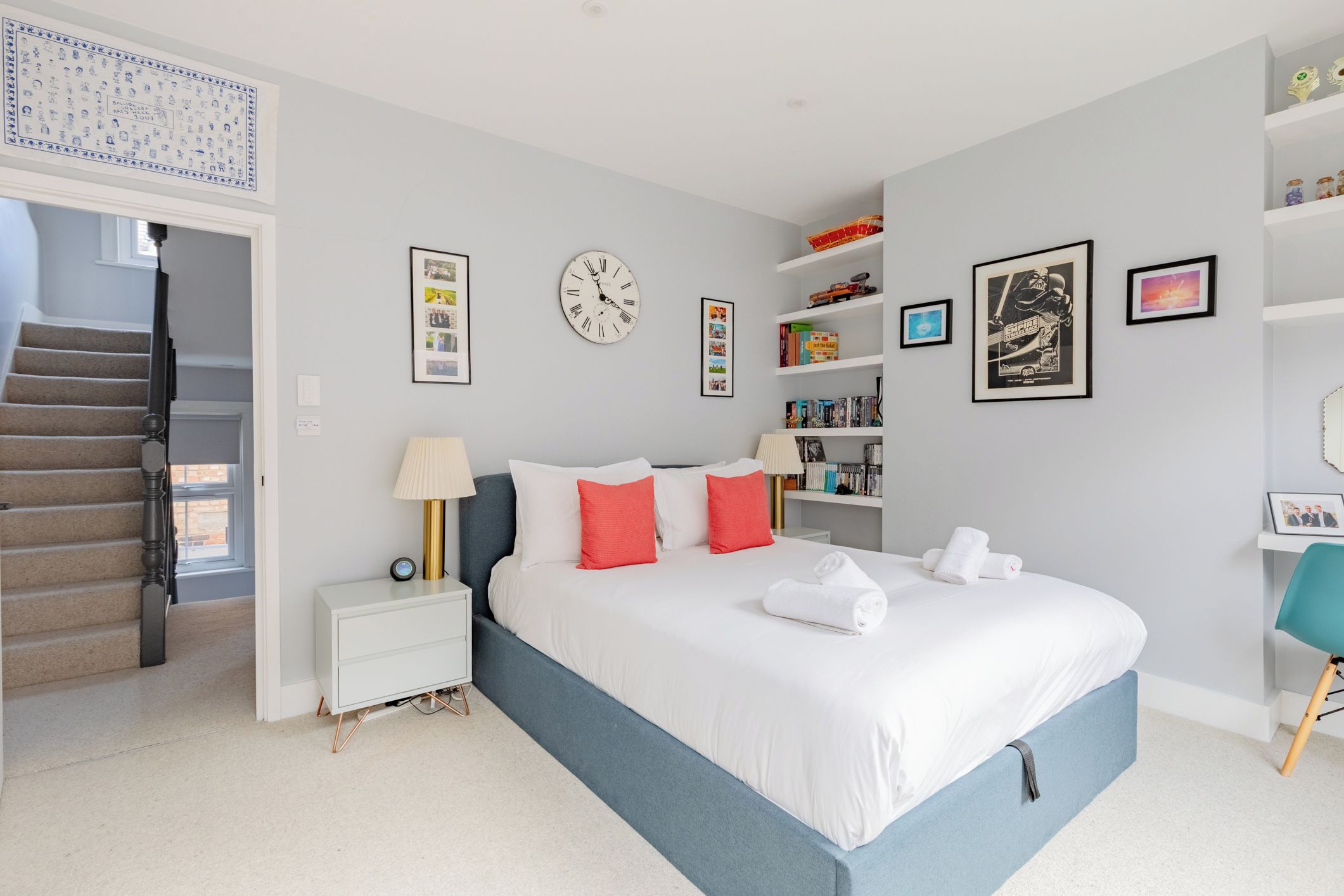 A bedroom with a bed, nightstands, a lamp, a clock, and a bookshelf.
