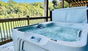 A hot tub with a control panel, surrounded by a wooden deck and a view of a forested area. - Fall is in the air, 2 full kitchens . Bring the whole family . (Sevierville)