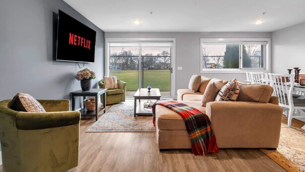 Ein Wohnzimmer mit einer Couch, einem Sessel und einem Couchtisch. Ein Flachbildfernseher ist an der Wand befestigt.