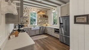 A modern kitchen with a stone backsplash, wooden cabinets, and a stainless steel refrigerator. - Hemlock Mist: Modern Lakeside Home w/  Screened Porch, Kayak (Highlands)