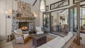 A cozy living room with a stone fireplace, wicker furniture, and a large glass door leading to an outdoor area. - Hemlock Mist: Modern Lakeside Home w/  Screened Porch, Kayak (Highlands)