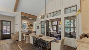 A spacious dining area with a large wooden table, multiple chairs, and a view of the outdoors through large windows. - Hemlock Mist: Modern Lakeside Home w/  Screened Porch, Kayak (Highlands)