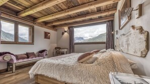 A bedroom with a wooden ceiling, a large bed with fluffy bedding, a sofa, and a view of mountains through the windows. - Ski-in-ski-out 4/5-bedroom chalet loft with jacuzzi in Les Houches, Chamonix (Les Houches)