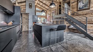 A modern kitchen with a central island, wooden beams on the ceiling, and a staircase leading to an upper level. - Ski-in-ski-out 4/5-bedroom chalet loft with jacuzzi in Les Houches, Chamonix (Les Houches)