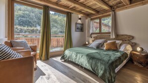 A bedroom with a wooden ceiling, a bed with a green blanket, a wooden headboard, and a view of a wooden deck and trees. - Ski-in-ski-out 4/5-bedroom chalet loft with jacuzzi in Les Houches, Chamonix (Les Houches)
