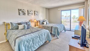 A bedroom with two beds, a desk, a computer, and a window with a view.