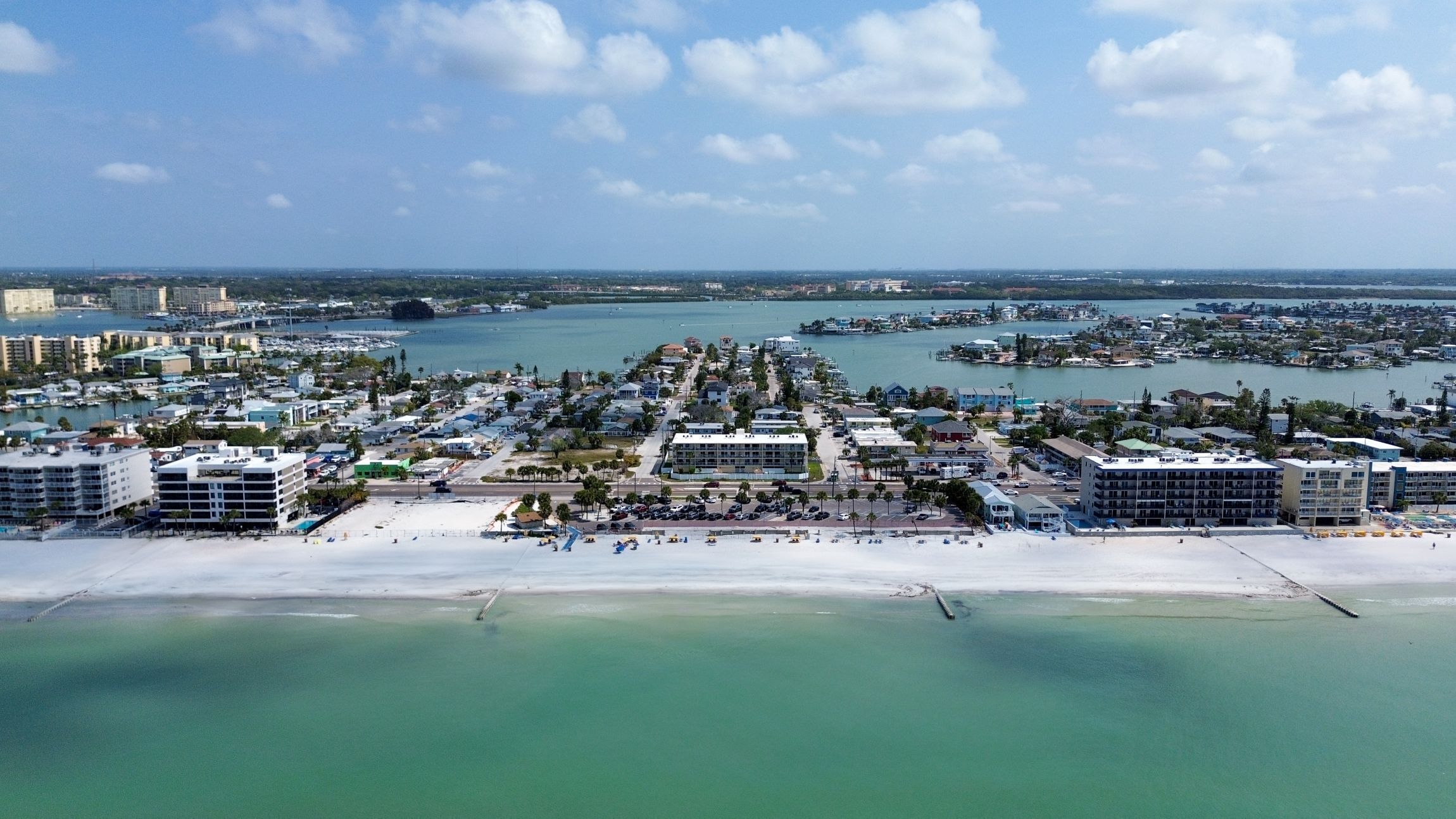 An aerial view of a coastal town with a beach, marina, and residential buildings.