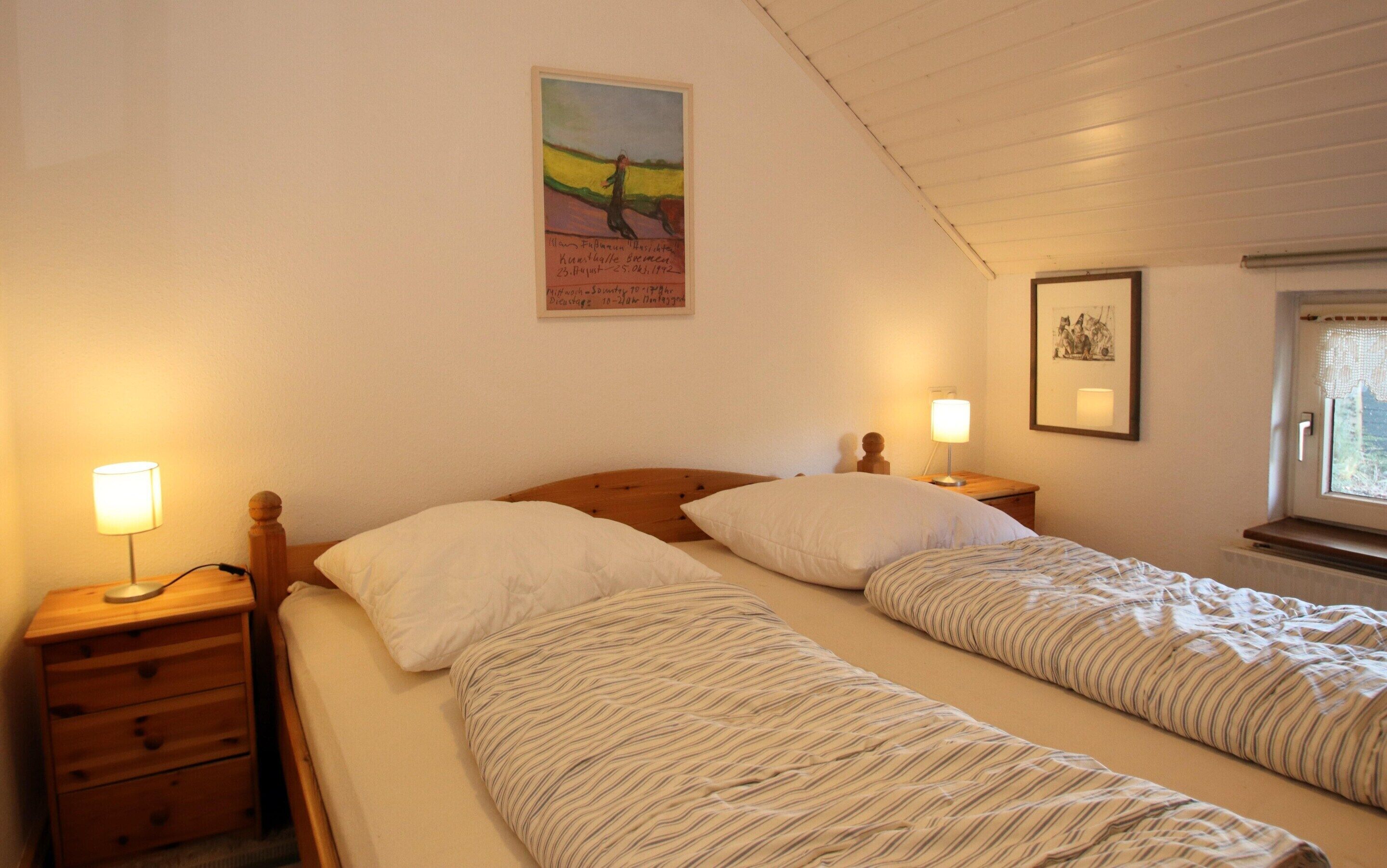 Un dormitorio con dos camas individuales, cabeceros de madera, mesitas de noche con lámparas y un cuadro en la pared.