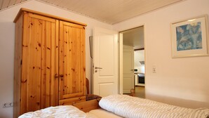 A bedroom with two beds, a wooden wardrobe, and a door leading to a bathroom. - Ferienwohnung im Reetdachhaus, Burhave (Butjadingen)