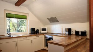 A modern kitchen with white cabinets, a wooden countertop, a built-in oven, and a window with blinds. - Ferienwohnung im Reetdachhaus, Burhave (Butjadingen)