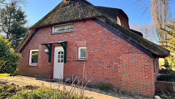 A brick building with a thatched roof, a white door, and two windows. - Ferienwohnung im Reetdachhaus, Burhave (Butjadingen)