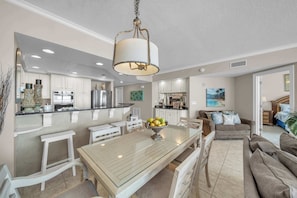 A spacious kitchen with white cabinetry, a central island with a bowl of fruit, and a dining area with a glass table.