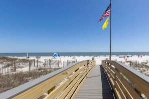 A wooden boardwalk leading to a beach with an American flag and a yellow flag.