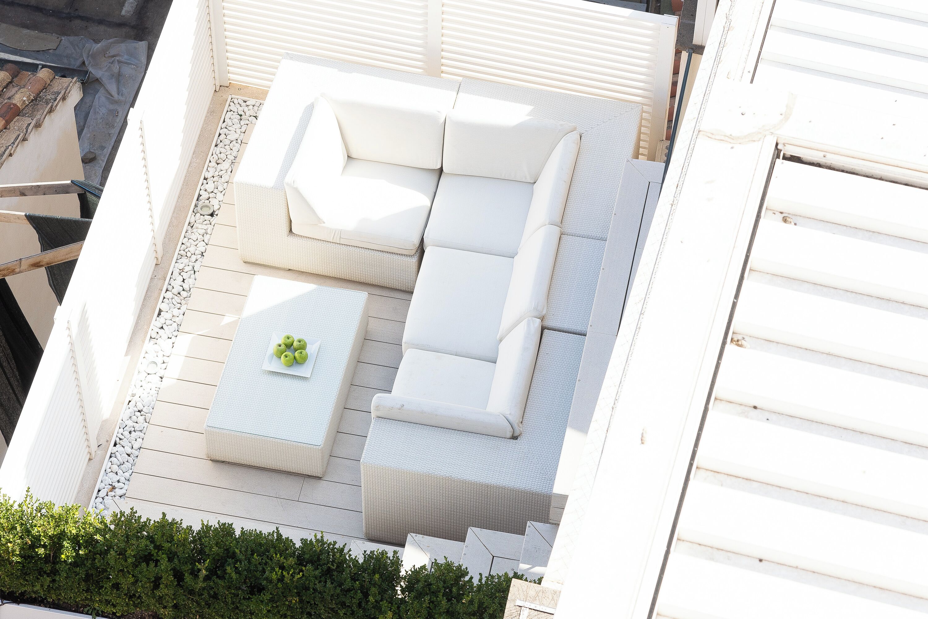 Un espace extérieur aménagé avec un canapé blanc et une petite table, entouré de murs blancs et d’une terrasse en bois.