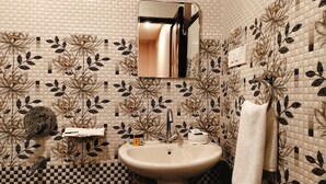 Een badkamer met een wastafel, spiegel en betegeling met bloemmotieven.