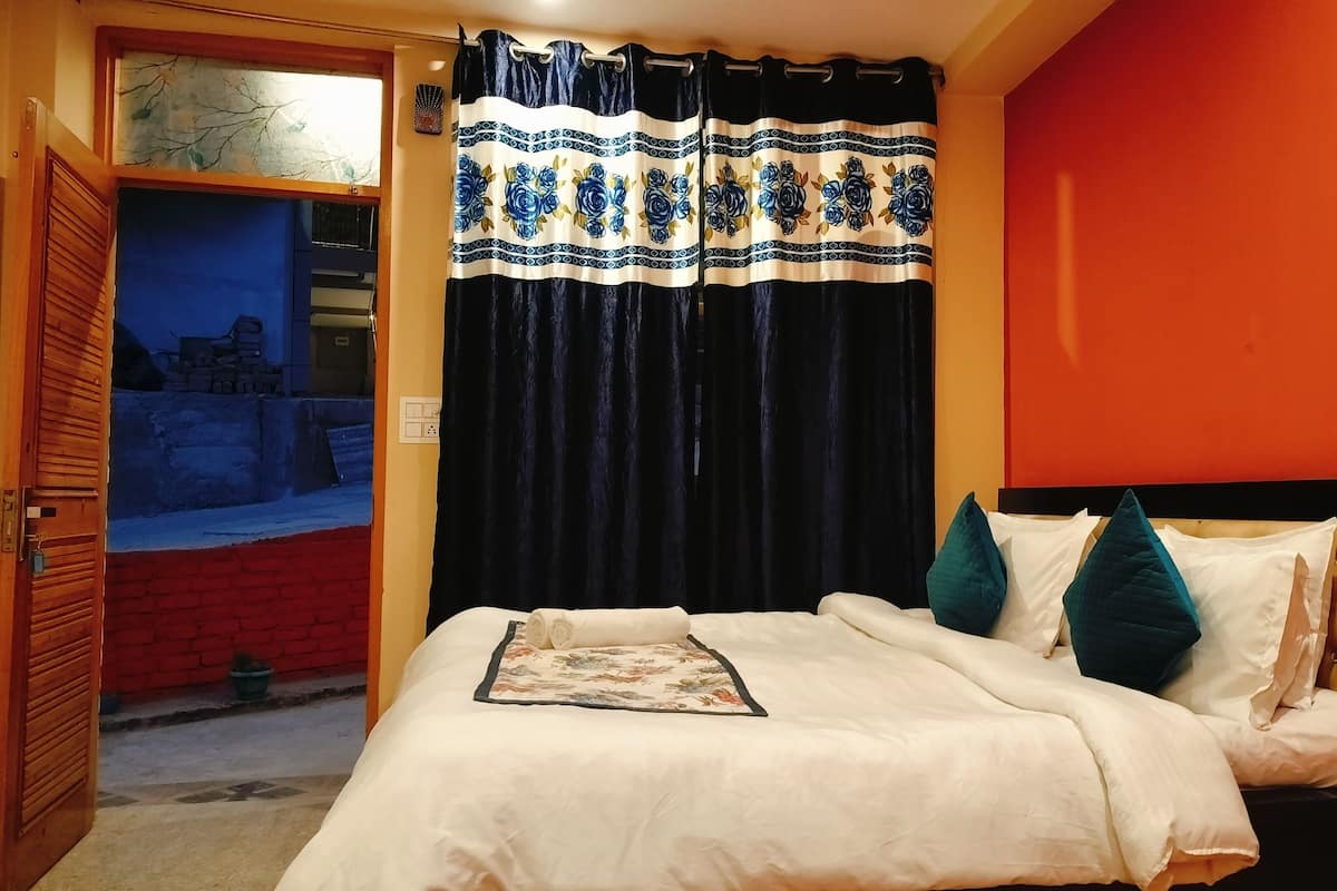 Un dormitorio con cama, ventana con vista a un muro de ladrillo y cortina estampada con motivos florales.