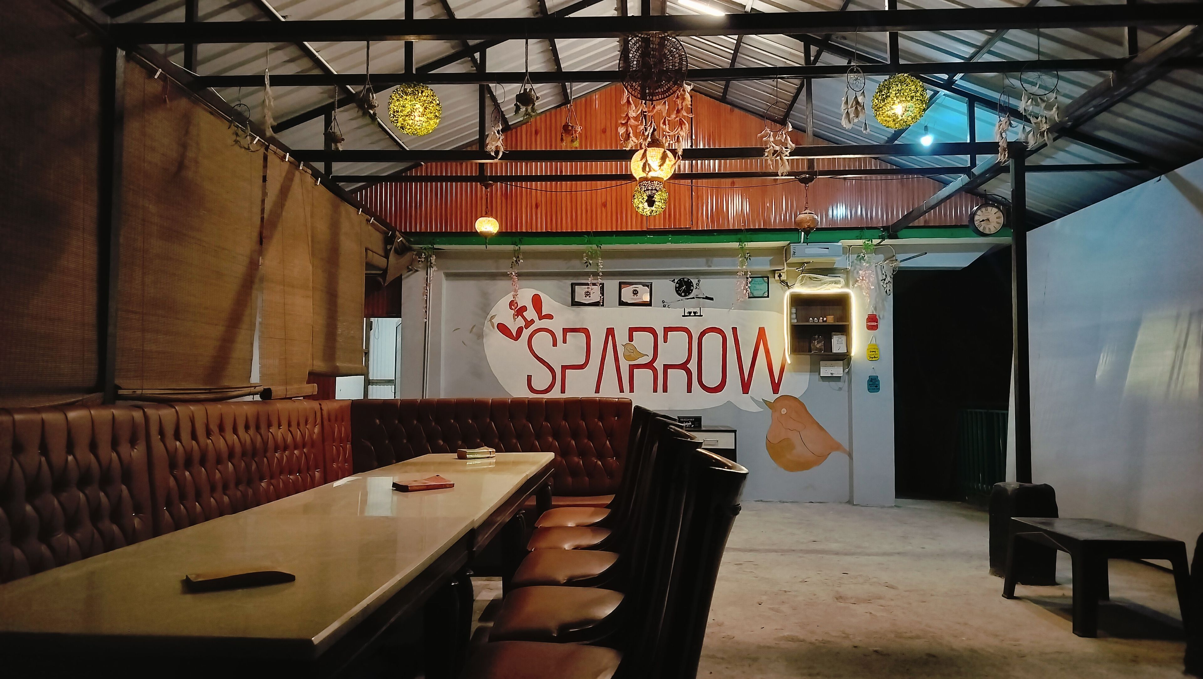 Interior de un restaurante con techo alto, adornos colgantes y un letrero en la pared que dice 'SPARROW'.