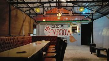 Interior de un restaurante con techo alto, adornos colgantes y un letrero en la pared que dice 'SPARROW'.
