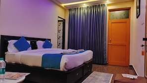 Ein Hotelzimmer mit einem Bett, einem Nachttisch, einer Tür und einem Fenster mit Vorhängen.