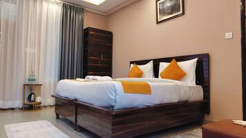 A neatly made bed with a wooden headboard, a bedside table with a bottle and a cup, and a large window with curtains.