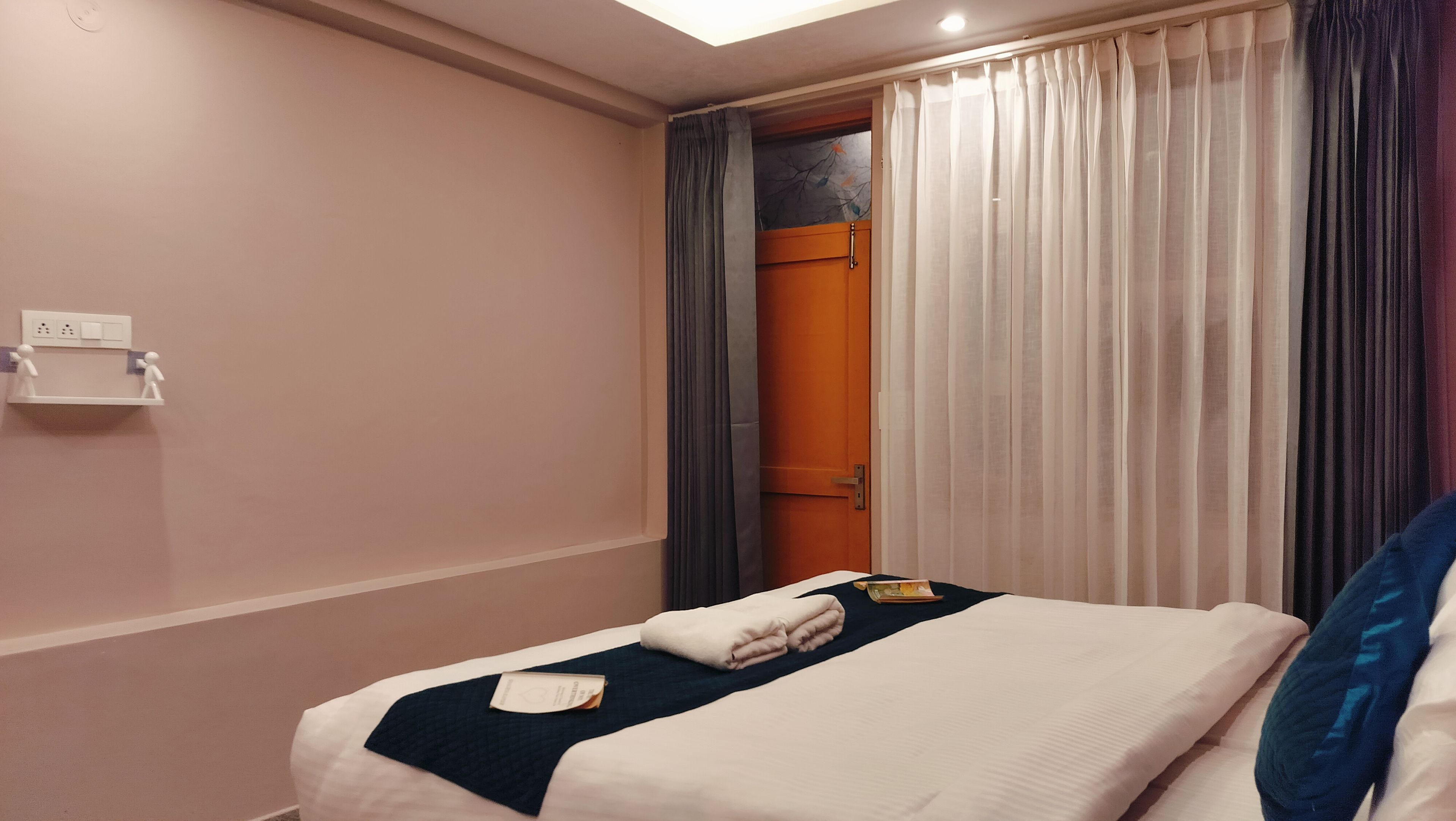 A hotel room with a bed, a nightstand, a window with curtains, and a door.