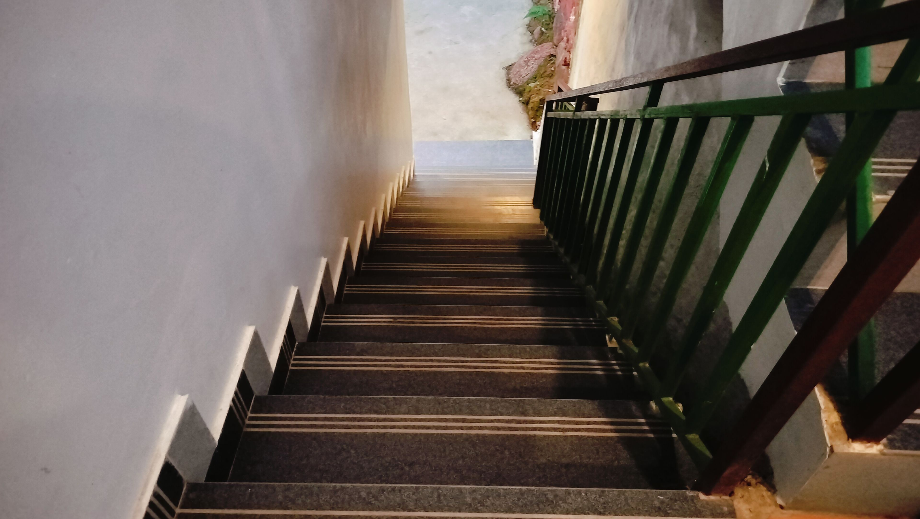 A staircase with a green metal railing and a white wall on one side.