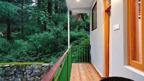 A balcony with a stone wall, a green railing, and a view of dense greenery.