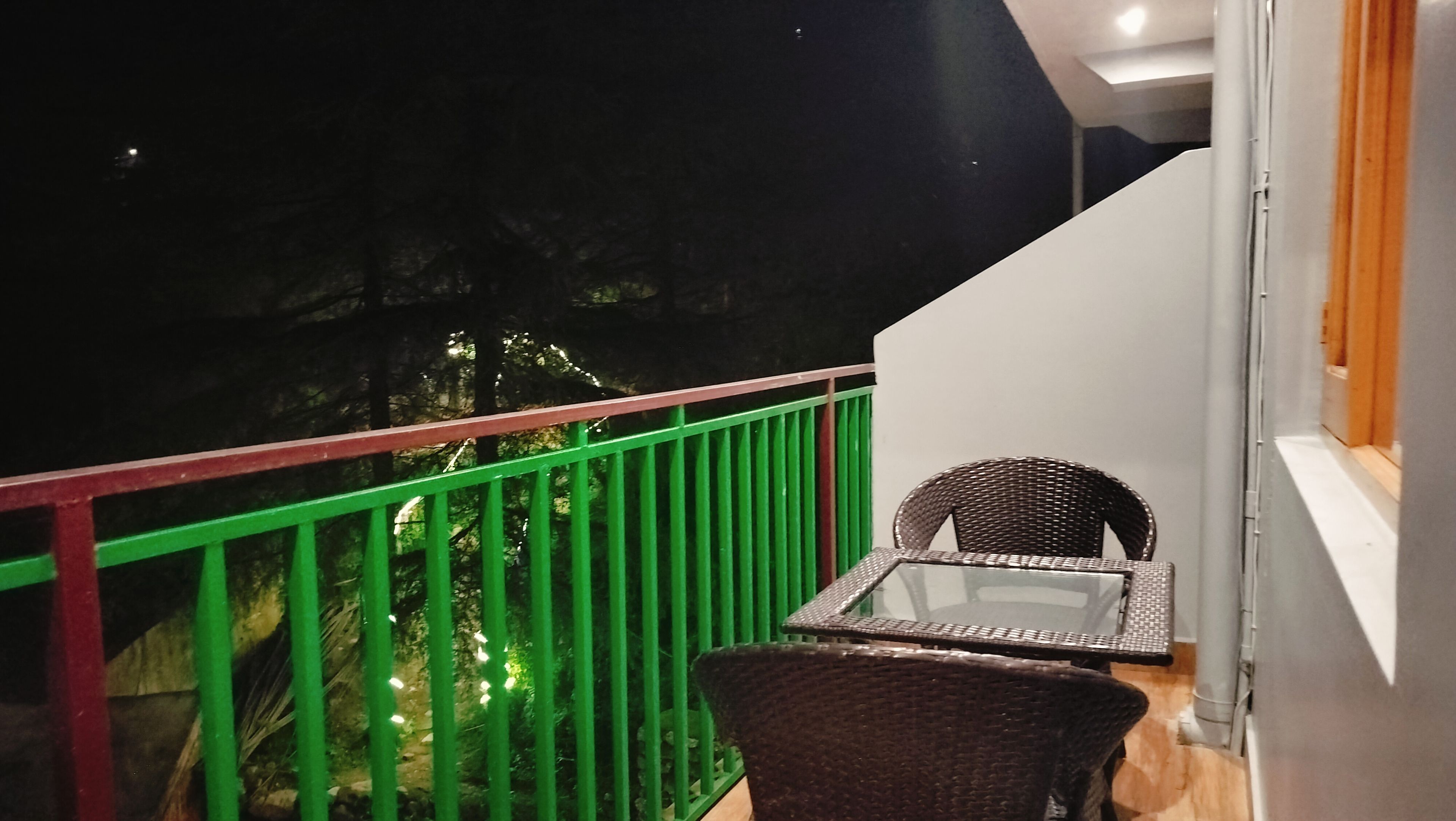 A balcony with a green railing, a wicker chair, and a table.