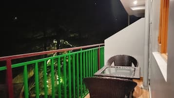 A balcony with a green railing, a wicker chair, and a table.