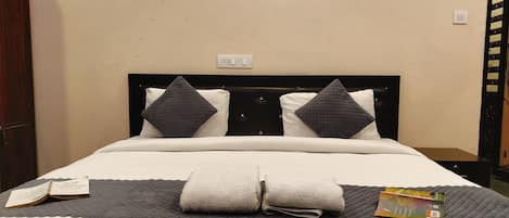 A hotel room with a bed, pillows, a bedside table, a book, and a power outlet.