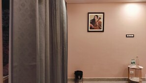 Ein Zimmer mit einem gerahmten Kunstwerk an der Wand, einem kleinen Tisch mit Flaschen und einem Mülleimer.