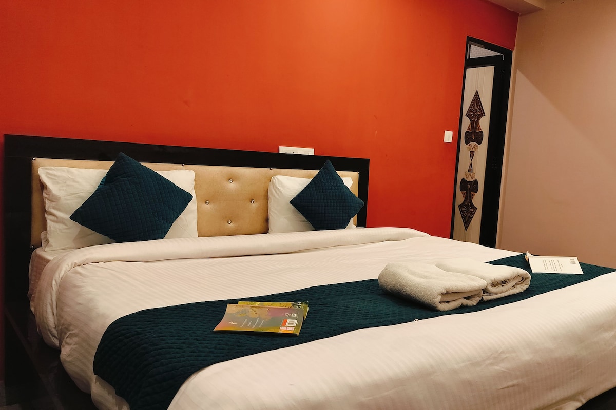 Una cama bien hecha con una colcha blanca y azul turquesa, dos almohadas azules y una toalla doblada al lado.