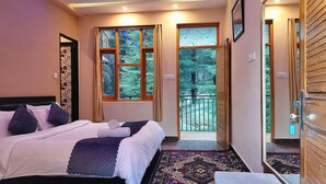 Hotelkamer met een bed, een zithoekje, een balkon met uitzicht op bomen en een deur naar buiten.