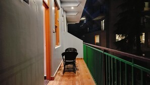A corridor with a chair, a green railing, and a staircase leading to an upper level. - Lill sparrow by The Verdant Escapes (Dharamshala)