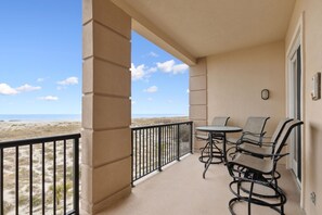Un balcon avec vue sur la plage, une table avec des chaises et une petite fenêtre.