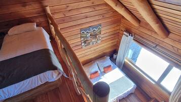 Una cabaña de madera con un entrepiso que tiene dos camas, una ventana y techo de madera.