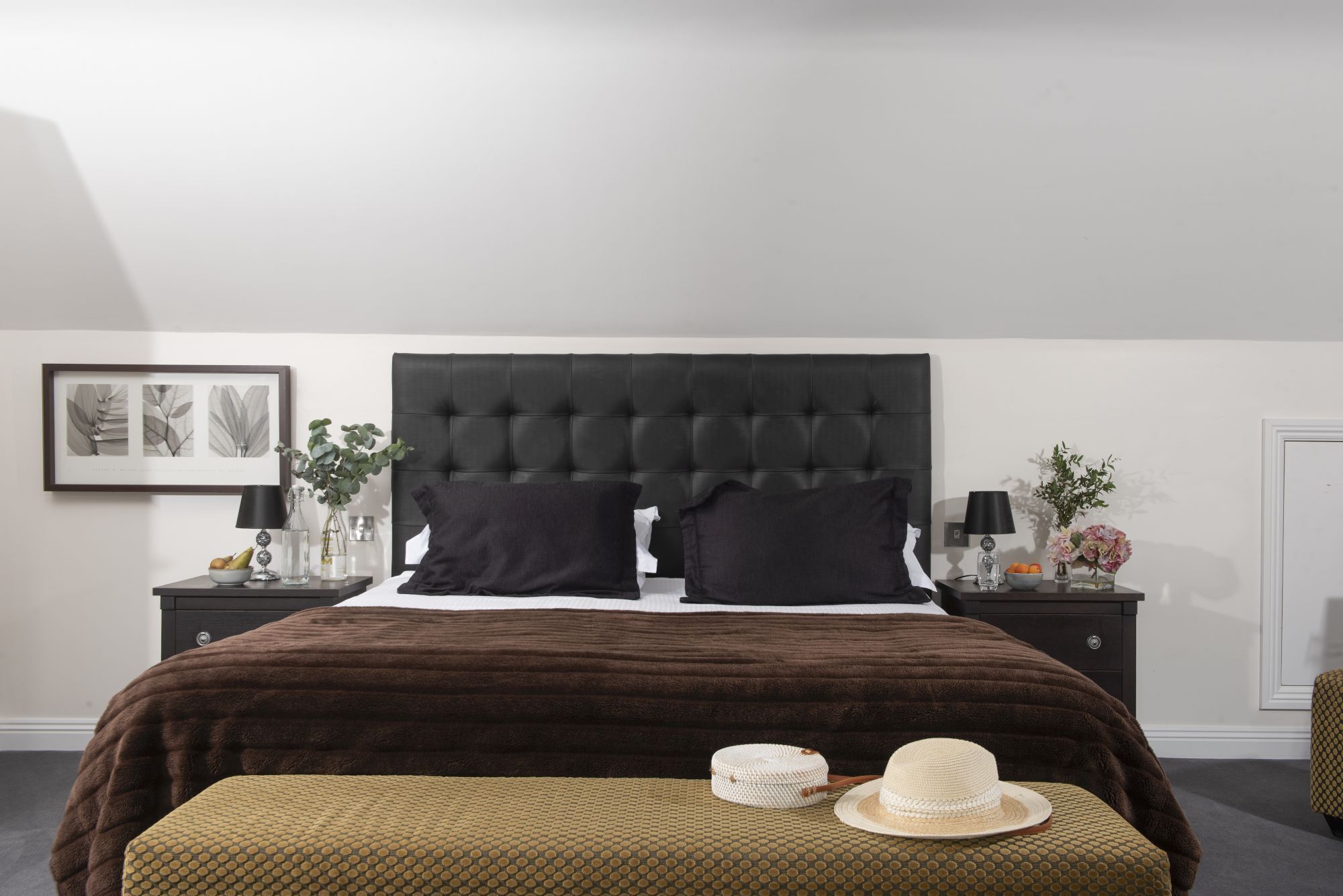 Un dormitorio con una cama grande, dos mesitas de noche, un banco y una puerta.