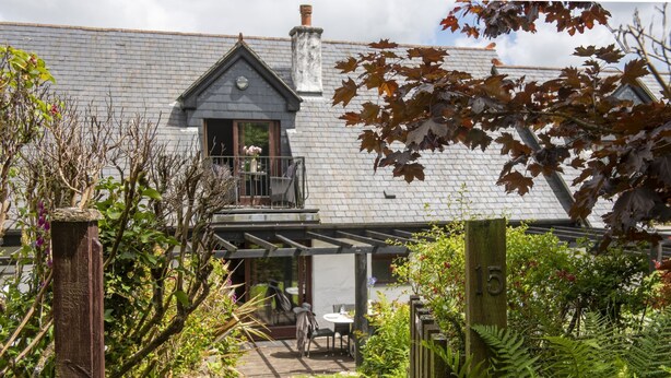 A house with a brick exterior, a balcony, and a garden with ferns and a wooden fence.