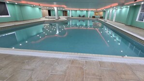 An indoor swimming pool with a tiled floor, surrounded by walls with windows and a ceiling with recessed lighting.