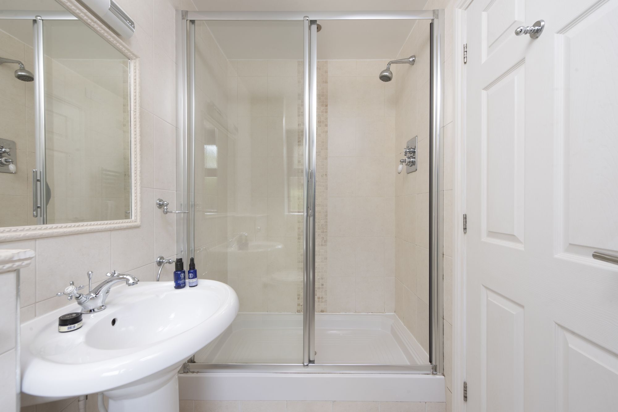 Une salle de bain moderne avec une douche à l’italienne, un lavabo blanc et une porte.