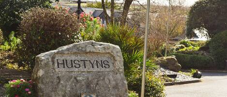 A stone sign with the name "Hustyns" surrounded by greenery and a street lamp.