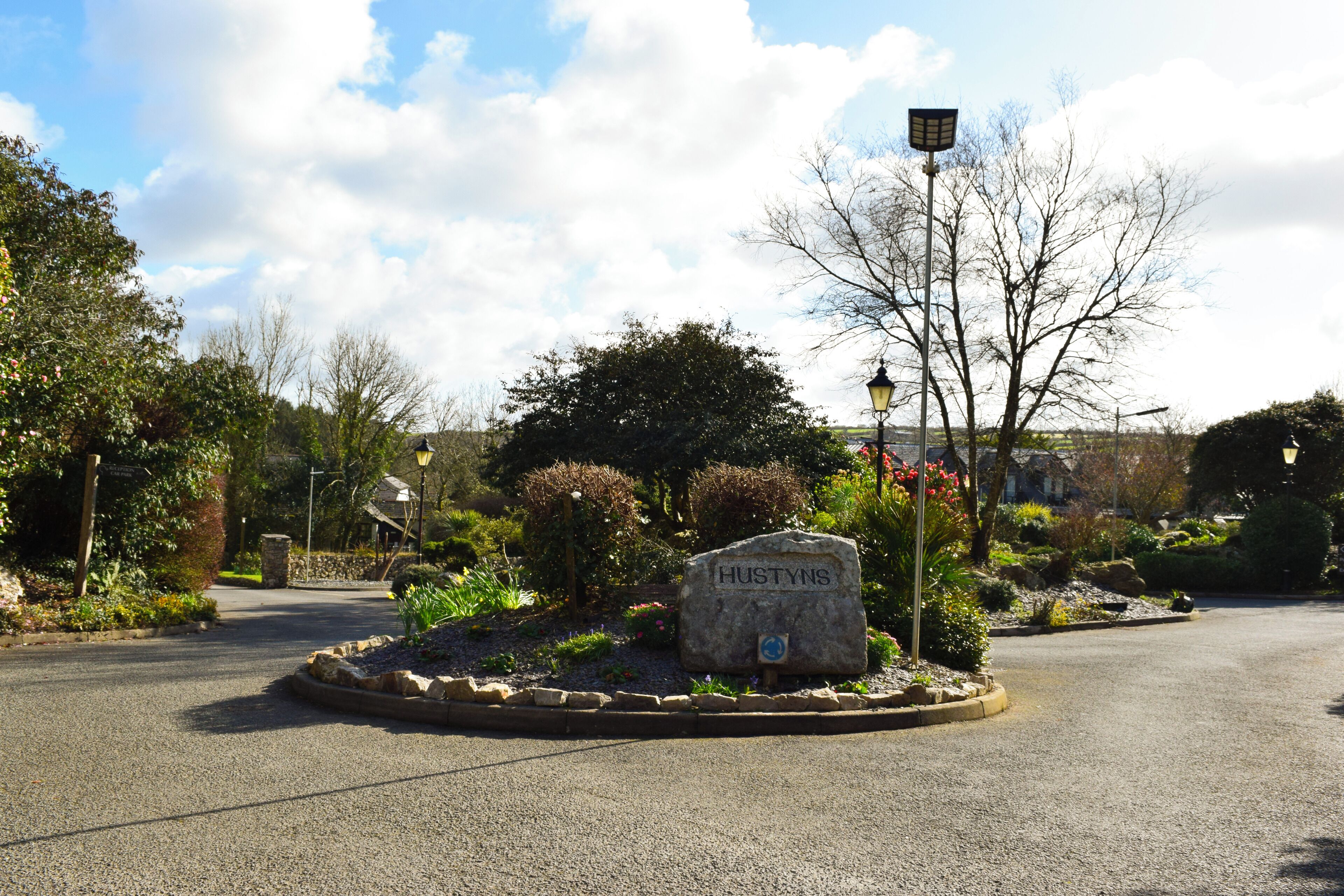 A landscaped area with a stone sign reading "HUSTYNS" surrounded by plants and a street lamp.