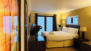 A hotel room with a bed, bedside table, lamp, and a vase with flowers.
