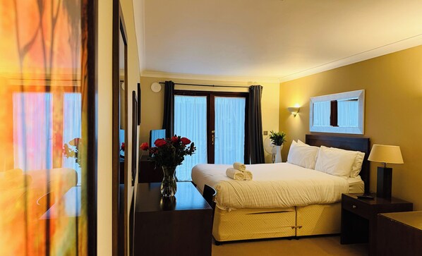 A hotel room with a bed, bedside table, lamp, and a vase with flowers. - Hustyns Hotel (Wadebridge)