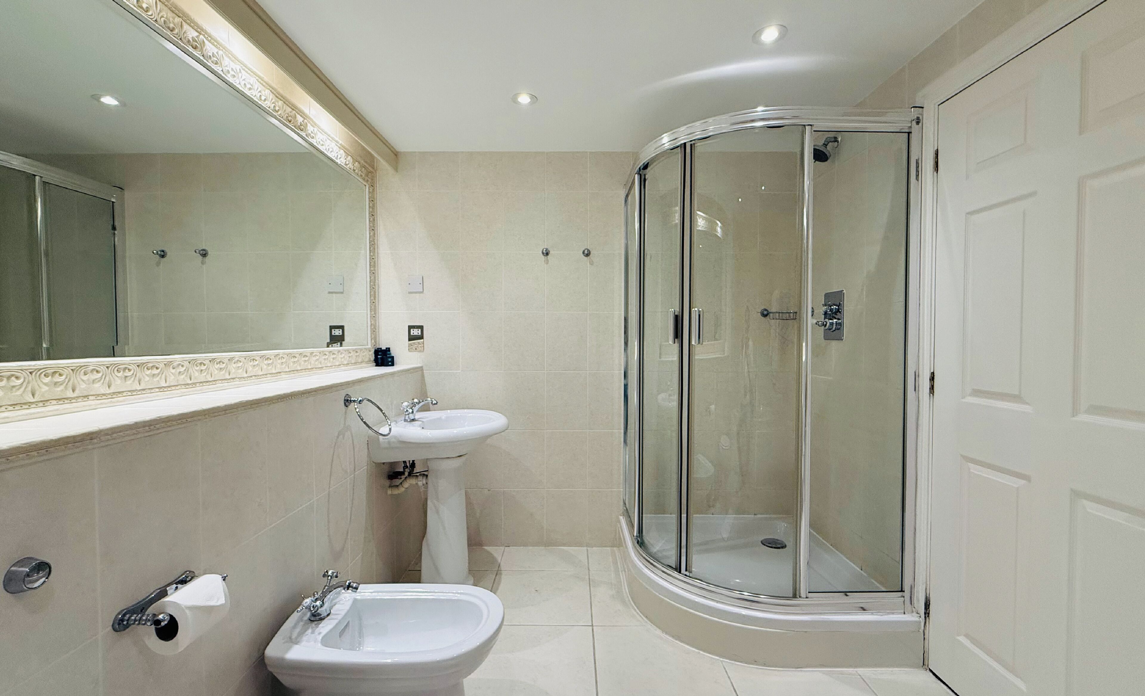 Un baño moderno con ducha de vidrio, lavamanos pedestal y retrete.