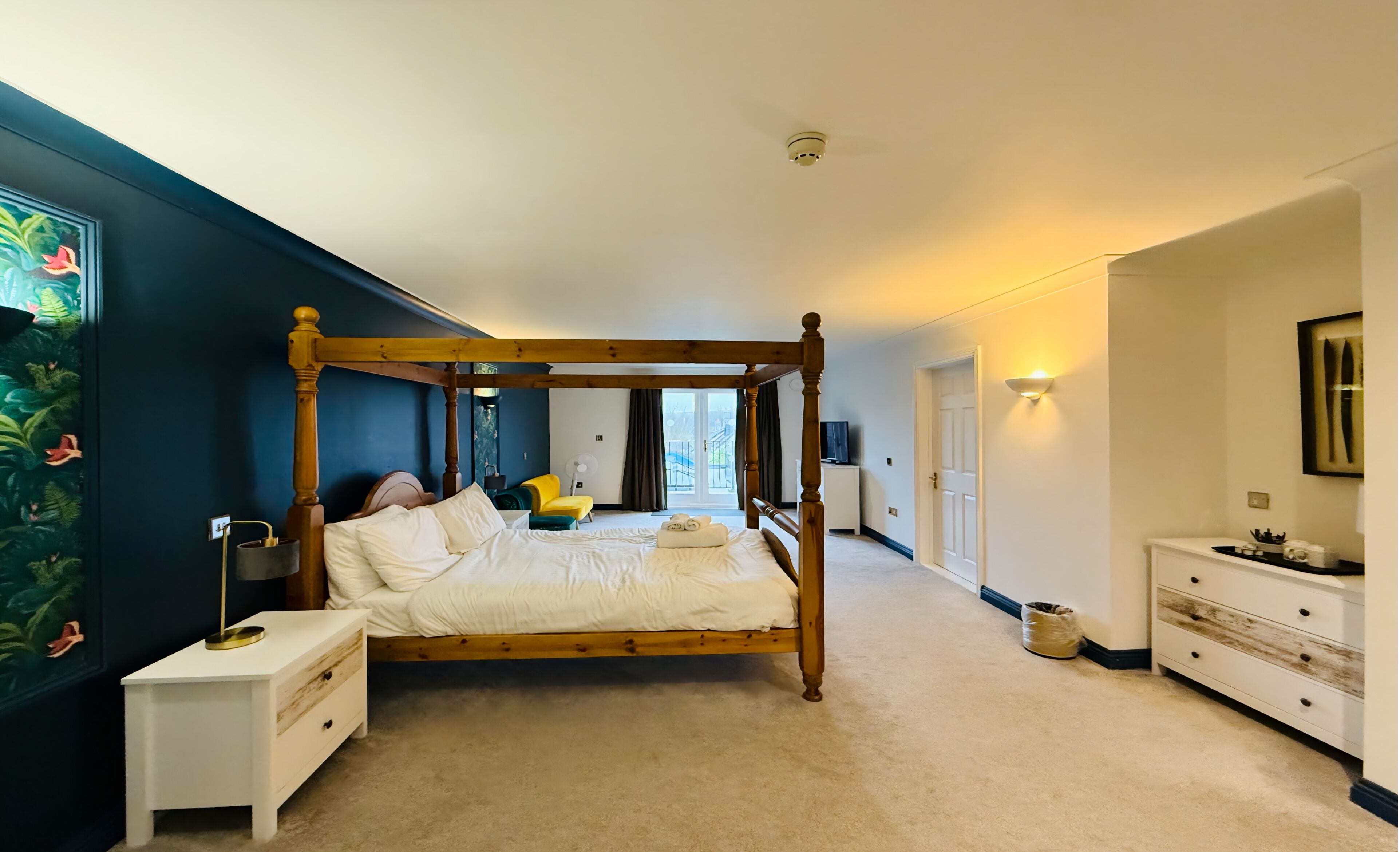 A four-poster bed in a bedroom with a nightstand, a dresser, and a painting on the wall.