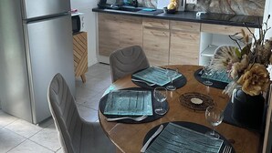 A modern kitchen with wooden cabinets, a built-in oven, and a dining area set with a table, chairs, and a vase of flowers. - Le Corossol (Fort-de-France)