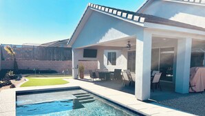Un área de piscina moderna al aire libre con agua azul cristalina, rodeada por un patio con sillas y una mesa.