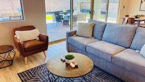 Una sala de estar moderna con un sillón de cuero marrón, un sofá gris y una mesa de centro redonda con una planta.